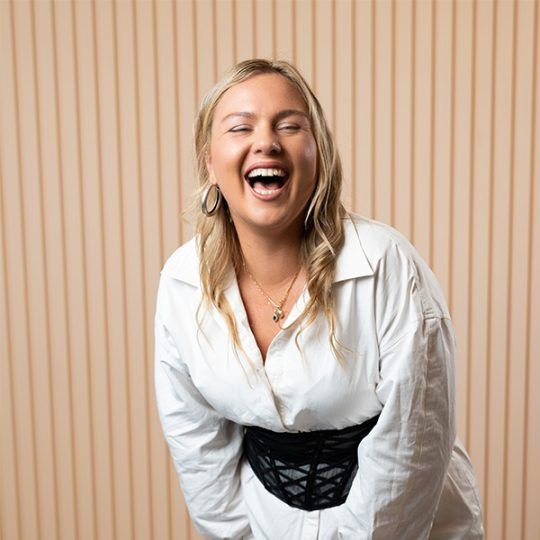 Staff member Phia. A young woman with blonde hair. She is leaning forward and laughing.